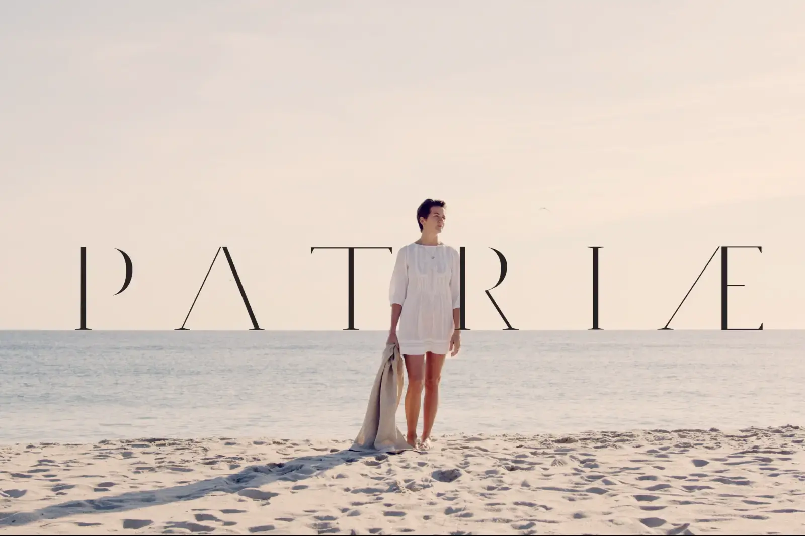 Woman on beach wearing white linen dress with Patriae logo overlay